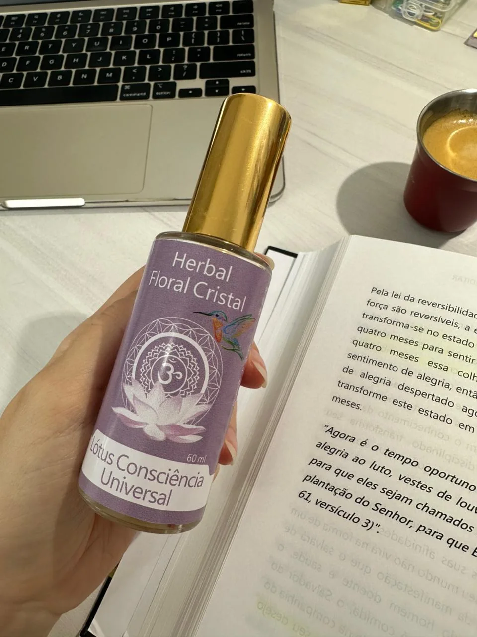 Frasco de perfume áurico vibracional segurado na mão, sobre um livro aberto