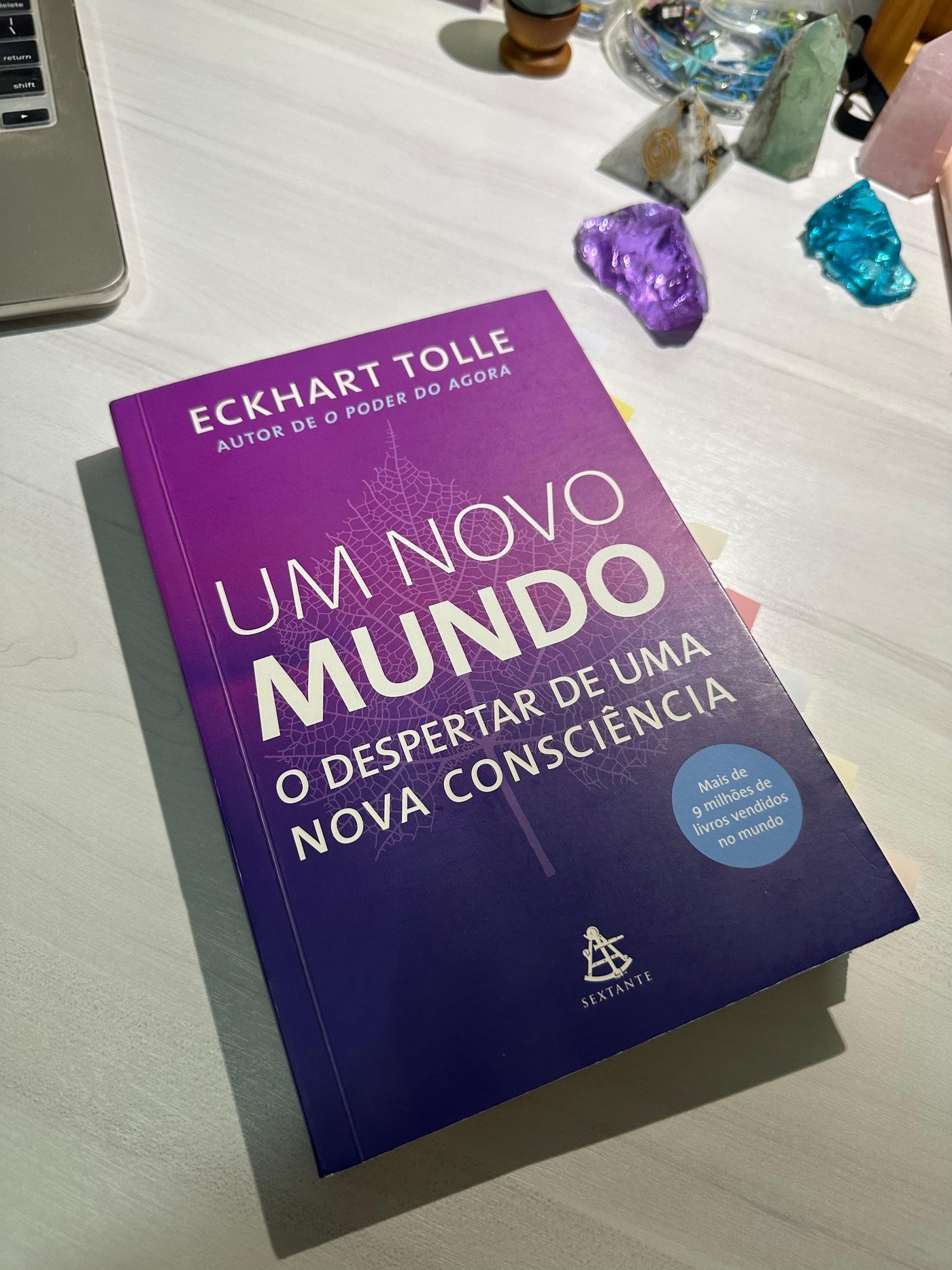 O livro Um Novo Mundo sobre a mesa, ao lado de cristais